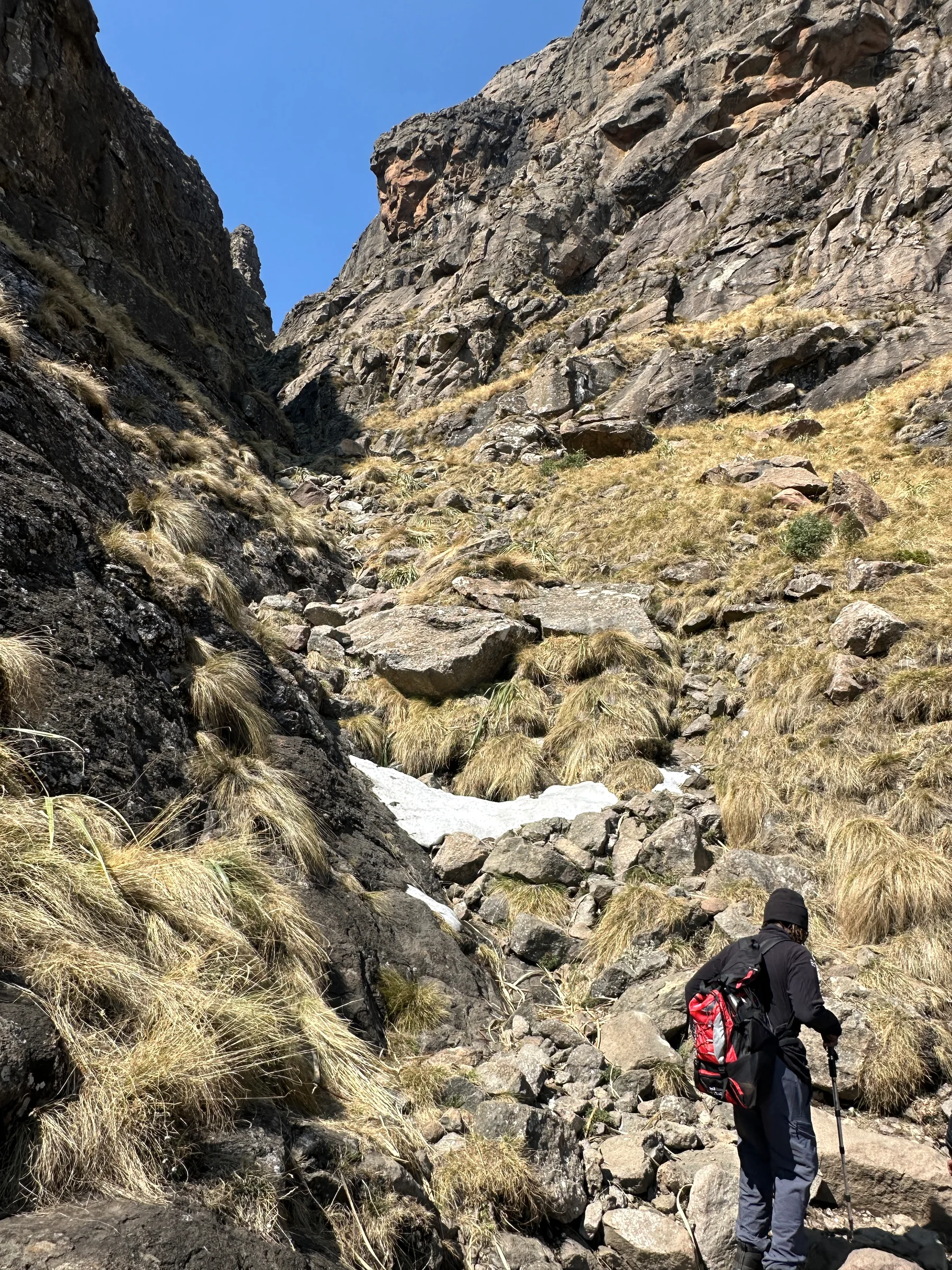 A hiker with a red and black backpack ascending a rocky gully