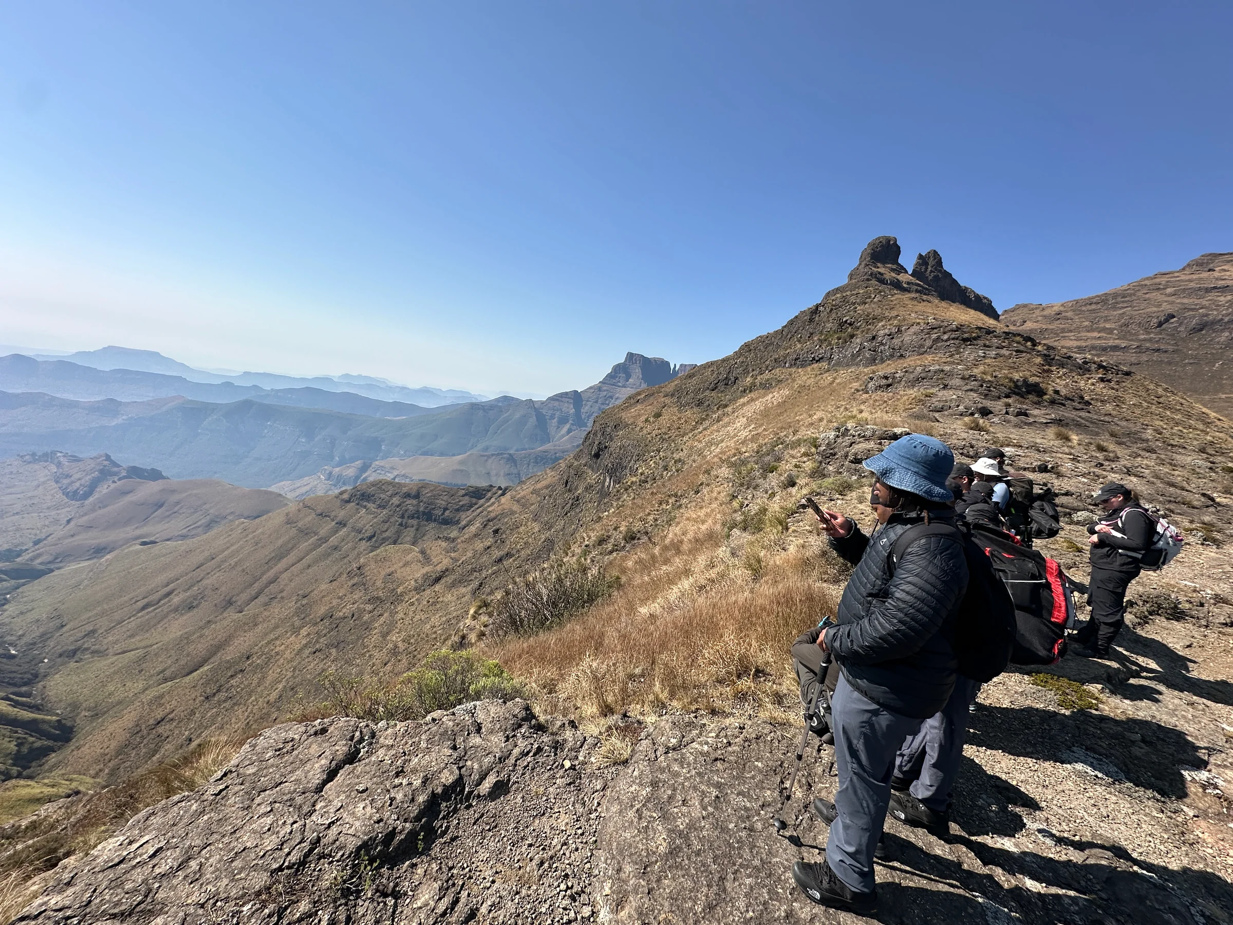 Hikers pausing on a rocky ridge with a wide valley behind them