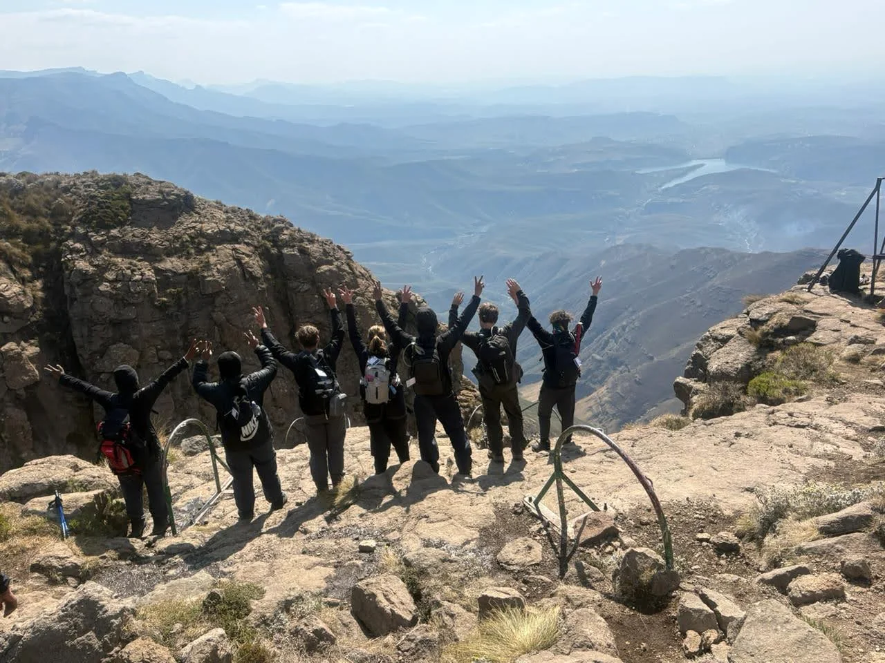 Hikers raising their arms above a broad mountain valley