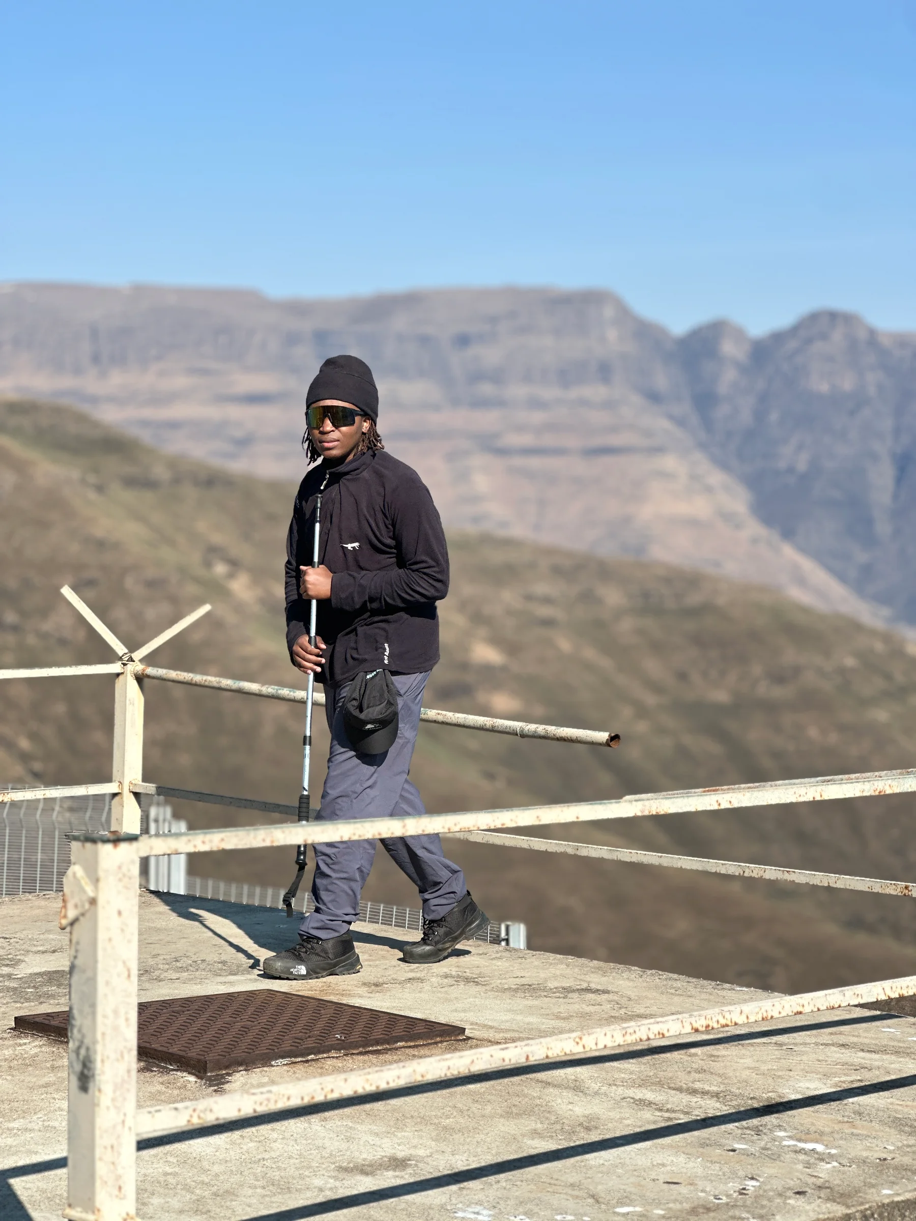 A hiker with trekking poles at a mountain lookout railing