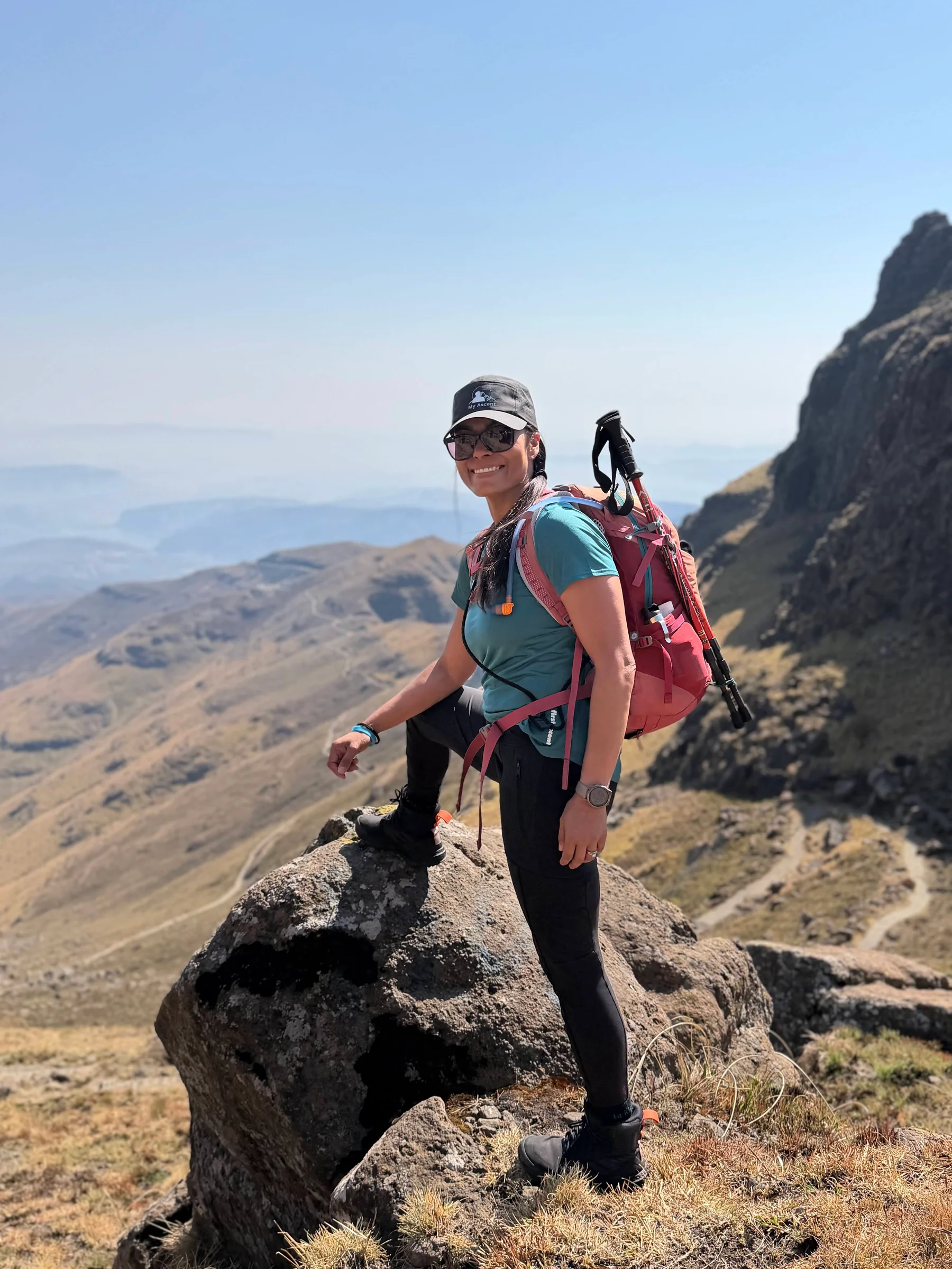 A hiker with a red backpack standing beside a rock above a valley