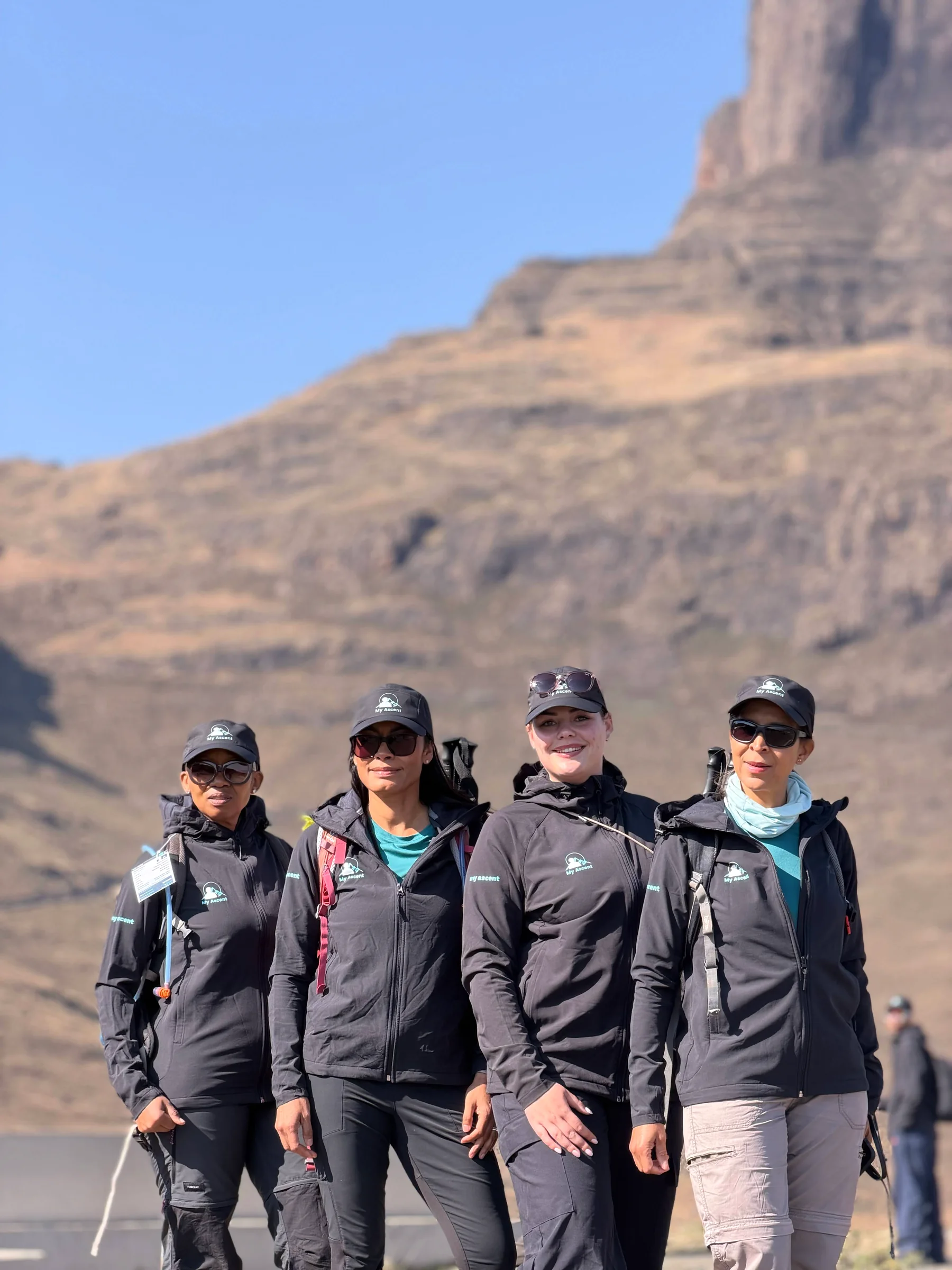 Four hikers posing together beneath rocky mountain cliffs
