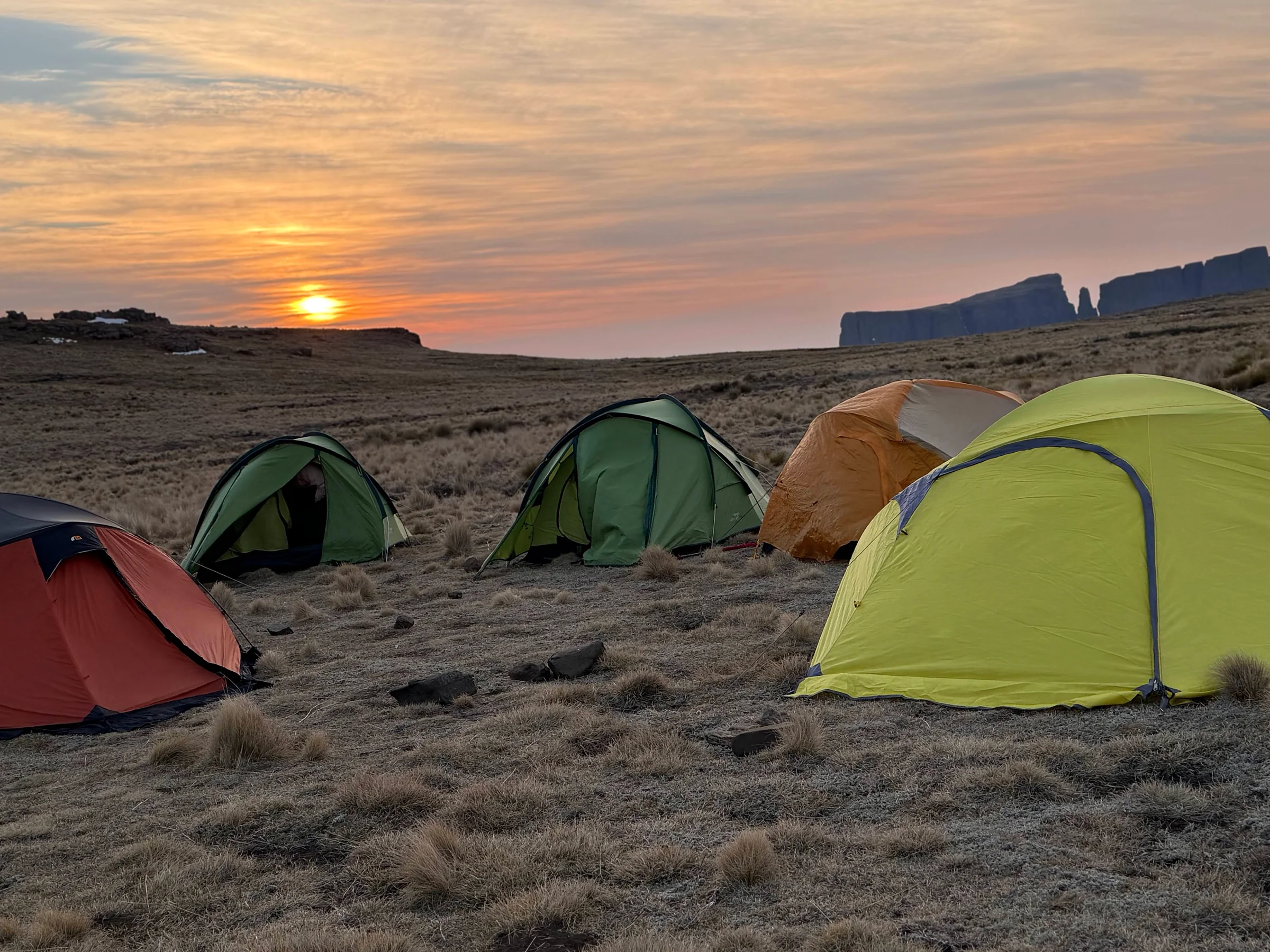 Colourful tents on mountain grassland beneath a golden sunset
